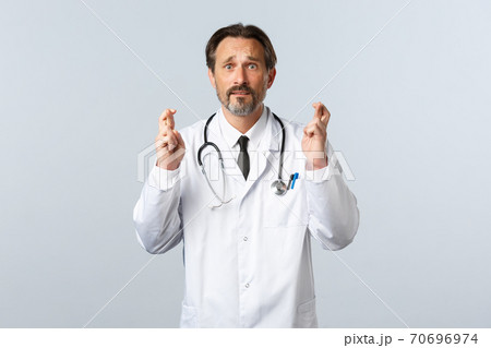 Covid-19, coronavirus outbreak, healthcare workers and pandemic concept. Hopeful anxious male doctor pleading desperate, cross fingers good luck, making wish as feeling worried Covid-19, coronavirus outbreak, healthcare workers and pandemic concept. Hopeful anxious male doctor pleading desperate, cross fingers good luck, making wish as feeling worried 70696974