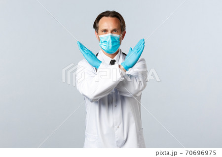 Covid-19, preventing virus, healthcare workers and vaccination concept. Serious determined doctor fighting coronavirus tell what not do, cross arms in stop or prohibition gesture Covid-19, preventing virus, healthcare workers and vaccination concept. Serious determined doctor fighting coronavirus tell what not do, cross arms in stop or prohibition gesture 70696975