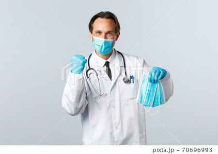 Covid-19, preventing virus, healthcare workers and vaccination concept. Cheerful doctor in clinic wearing PPE received medical masks for hospital employees, standing white background Covid-19, preventing virus, healthcare workers and vaccination concept. Cheerful doctor in clinic wearing PPE received medical masks for hospital employees, standing white background 70696993
