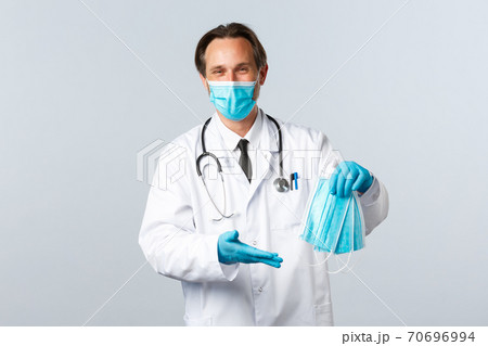Covid-19, preventing virus, healthcare workers and vaccination concept. Cheerful doctor in clinic wearing PPE received medical masks for hospital employees, standing white background 70696994