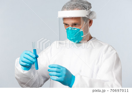 Covid-19, preventing virus, healthcare workers and vaccination concept. Serious-looking doctor in personal protective equipment carefully examine test tube with vaccine sample Covid-19, preventing virus, healthcare workers and vaccination concept. Serious-looking doctor in personal protective equipment carefully examine test tube with vaccine sample 70697011