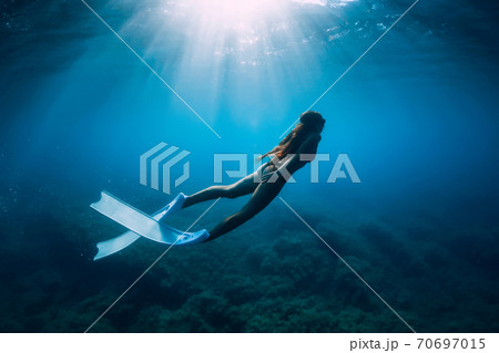 Free diver woman with white fins glides underwater with amazing sun rays. Freediving underwater Free diver woman with white fins glides underwater with amazing sun rays. Freediving underwater 70697015