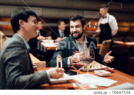 Men sit at the table and eat sushi and drink wine. 70697556