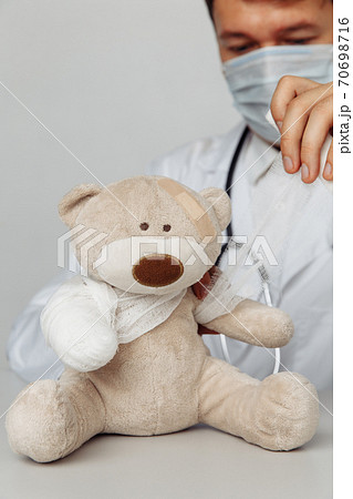 Pediatrician in mask bandage teddy bear in medical office. Close-up. Vertical image. Children healthcare concept 70698716