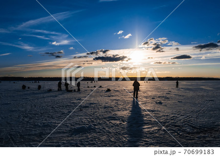silhouettes of fishermen fishing and ice screws in winter on the lake 70699183