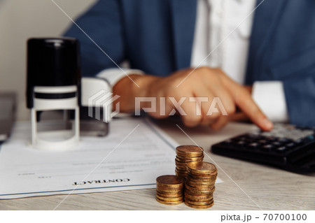 Man is counting profit on a calculator, stack of coins on desk in office. Economy and management financial concept 70700100