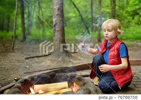 Little boy during family hiking plays with a burning stick by bonfire. Child having fun at camp fire Little boy during family hiking plays with a burning stick by bonfire. Child having fun at camp fire 70700750