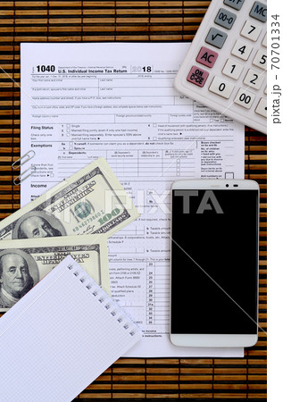 Composition of items lying on the 1040 tax form. Dollar bills, calculator, smartphone, paper clip and notepad. The time to pay taxes 70701334