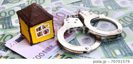 Small toy house and handcuffs is lies on a set of green monetary denominations of 100 euros. A lot of money forms an infinite heap Small toy house and handcuffs is lies on a set of green monetary denominations of 100 euros. A lot of money forms an infinite heap 70701579