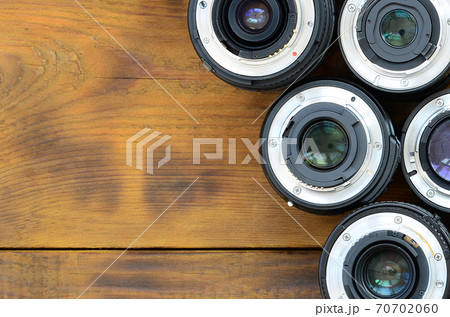 Several photographic lenses lie on a brown wooden background. Space for text 70702060