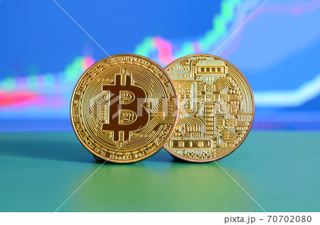 Two gold bitcoins lie on the green surface on the background of the display, which depicts the growth of the position on the chart 70702080