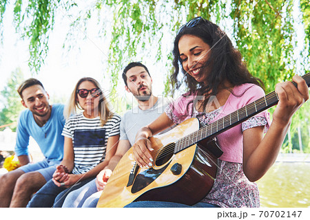 Group of happy friends with guitar. While one of them is playing guitar and others are giving him a round of applause Group of happy friends with guitar. While one of them is playing guitar and others are giving him a round of applause 70702147