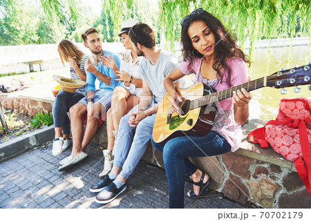 Group of happy friends with guitar. While one of them is playing guitar and others are giving him a round of applause 70702179
