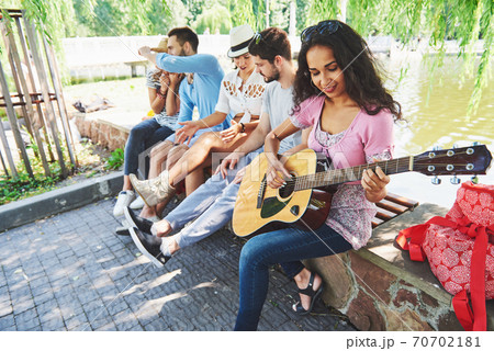 Group of happy friends with guitar. While one of them is playing guitar and others are giving him a round of applause 70702181