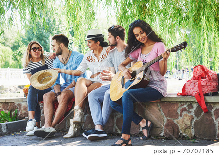 Group of happy friends with guitar. While one of them is playing guitar and others are giving him a round of applause 70702185