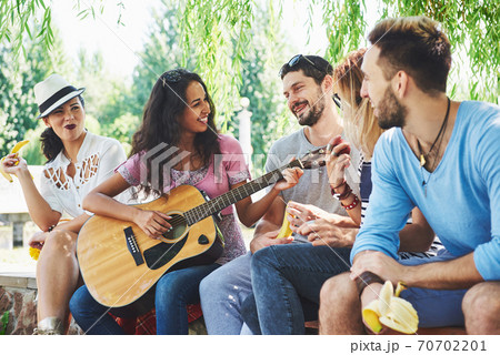 Group of happy friends with guitar. While one of them is playing guitar and others are giving him a round of applause 70702201