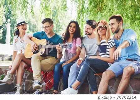 Group of happy friends with guitar. While one of them is playing guitar and others are giving him a round of applause 70702214