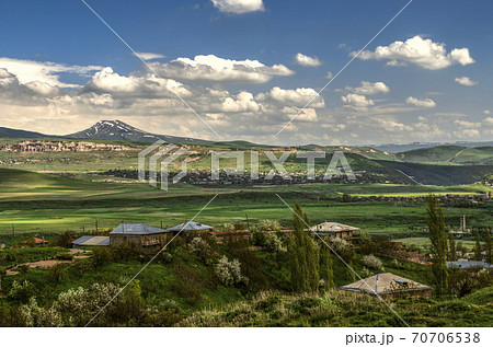 Village in the distance and Azhdahak mountain range on the background of spring blue sky with Cumulus clouds coming from the mountains in Armenia Village in the distance and Azhdahak mountain range on the background of spring blue sky with Cumulus clouds coming from the mountains in Armenia 70706538
