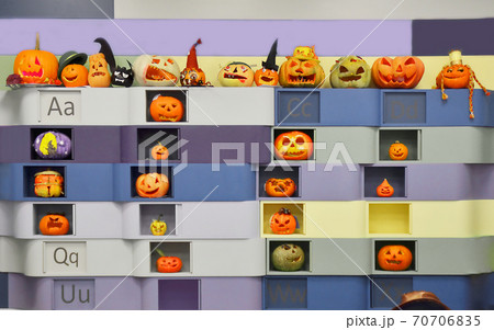 The wall with various halloween carved orange pumpkins crafted by children at the education school. Alphabet letters and funny faces The wall with various halloween carved orange pumpkins crafted by children at the education school. Alphabet letters and funny faces 70706835