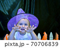 Halloween portrait of little girl wearing purple witch hat scaring the audience against black backgorund. Kid's custom of trick or treat. 70706839