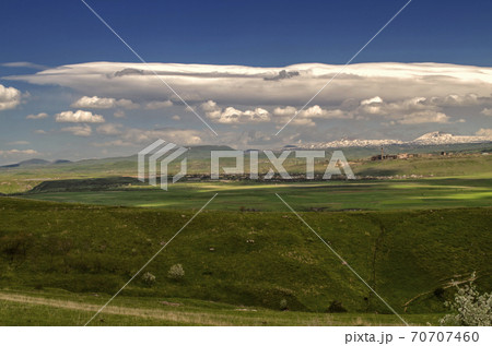 A blue sky with occasional turbulent clouds and Cumulus clouds is approaching the villages and valley of the Geghama mountains in Armenia 70707460