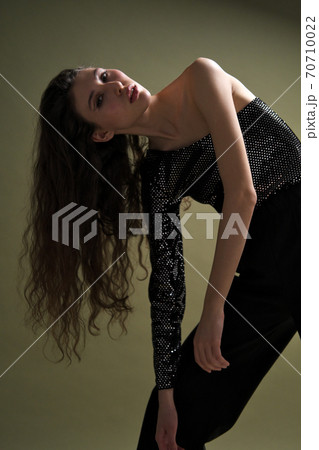 A beautiful young tall girl with long black hair poses in a shiny blouse and black culottes on a green background. Buty and fashion photo shoot. 70710022