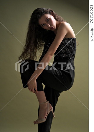 A beautiful young tall girl with long black hair poses in a shiny blouse and black culottes on a green background. Buty and fashion photo shoot. A beautiful young tall girl with long black hair poses in a shiny blouse and black culottes on a green background. Buty and fashion photo shoot. 70710023