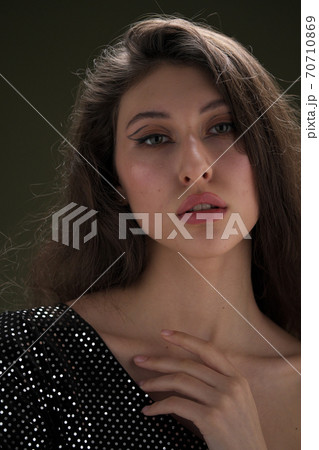 A beautiful young tall girl with long black hair poses in a shiny blouse and black culottes on a green background. Buty and fashion photo shoot. 70710869