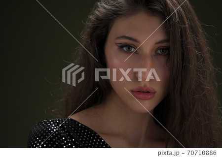 A beautiful young tall girl with long black hair poses in a shiny blouse and black culottes on a green background. Buty and fashion photo shoot. 70710886