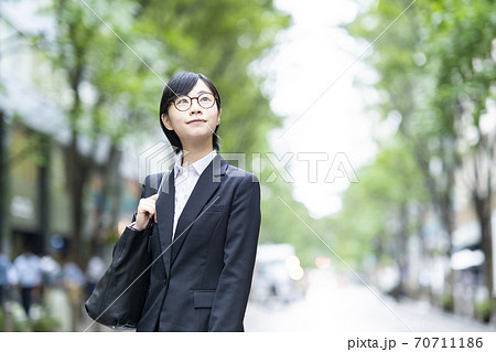 街路樹が並ぶ通りに立つスーツ姿の若い女性 街路樹が並ぶ通りに立つスーツ姿の若い女性 70711186