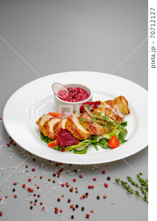 Chicken fillet in bacon with arugula and sauce on a white plate. 70712127