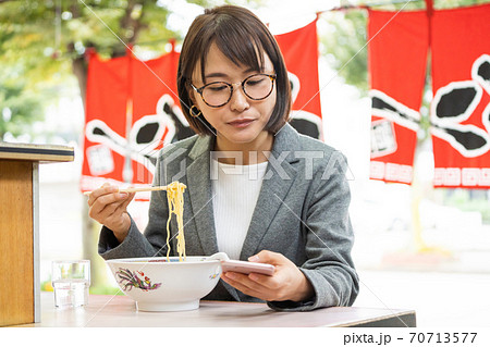 ラーメンを食べながらスマホを見る若い女性 70713577