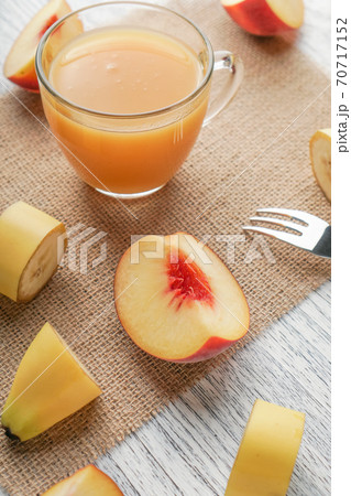 Glass of peach juice on a sackcloth on a white wooden table with sliced fruit and a fork. Fruit Diet Breakfast 70717152