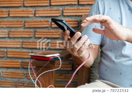 The hand of a man holding a smart phone and a modern Power Bank charger. Put it at the desk, charging the smartphone with a spare battery charger, In a size that sits play chair The hand of a man holding a smart phone and a modern Power Bank charger. Put it at the desk, charging the smartphone with a spare battery charger, In a size that sits play chair 70722532