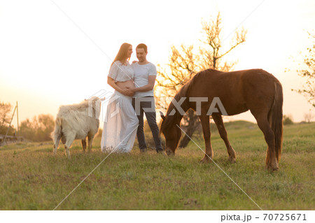 A farmer with his pregnant wife at sunset on his farm. Posing with their pets 70725671