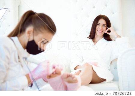 Pedicurist's hands in protective rubber gloves applying nail polish to the toenails Pedicurist's hands in protective rubber gloves applying nail polish to the toenails 70726223