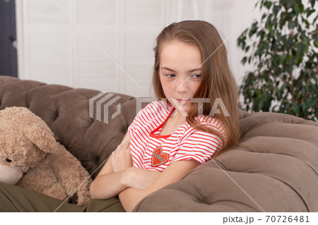 Portrait of a beautiful redhead teen girl. A sad girl in sadness sits on the couch with her arms crossed, does not smile, and does not look at the camera 70726481