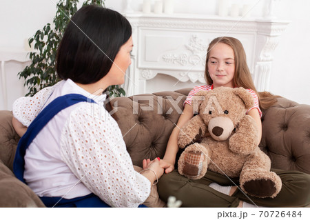 Teen girl on reception at the psychotherapist. Psychotherapy session for children. The psychologist works with the patient. Girl smiling sitting on a sofa next to a sitting female doctor therapist 70726484