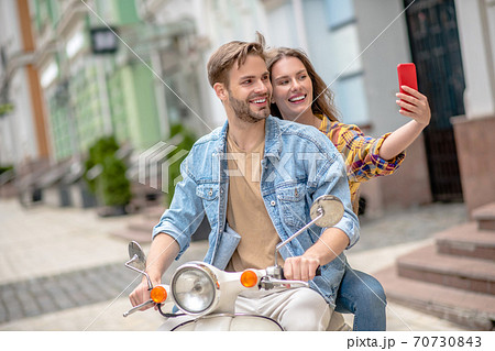 Woman taking a selfie while riding a scooter Woman taking a selfie while riding a scooter 70730843
