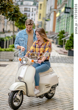 Man instructing woman to ride a scooter Man instructing woman to ride a scooter 70730856