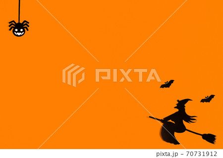Silhouettes of a flock of bats and a witch flying on a broom made of black paper on an orange 70731912