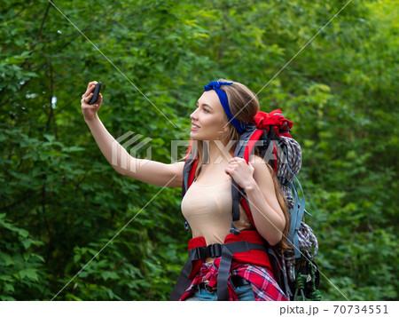 Smiling woman in the forest taking a selfie on a smartphone. 70734551