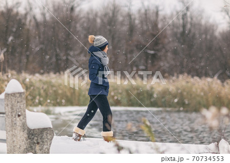 Winter snow storm happy cold weather girl walking in snowing forest woods background by the lake in cozy jacket 70734553