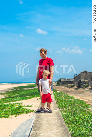 Father son walk along narrow concrete path, sea blue clear sky green grass background. Symbol as dad leads child into future adulthood. Happy childhood, fathers day, daddy influence on boy worldview 70735265