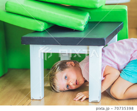 Cute little freckled face blond boy artistic facial expressions gestures, mischievous in good mood have fun at amusement playground entertainment center, hiding under the table. Happy childhood 70735398