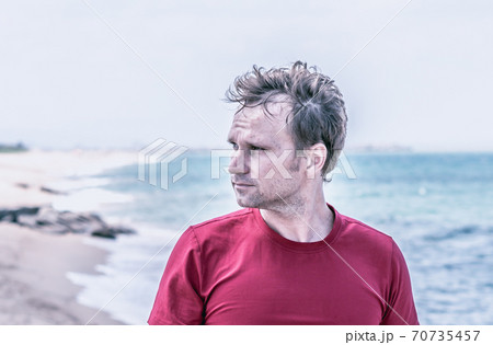 Serious handsome fair hair fluttering wind man red shirt, stubble face cheeks beard, wrinkled forehead sad, real skin, look far away thinking, blur sea skyline background BANNER. Life problems concept 70735457