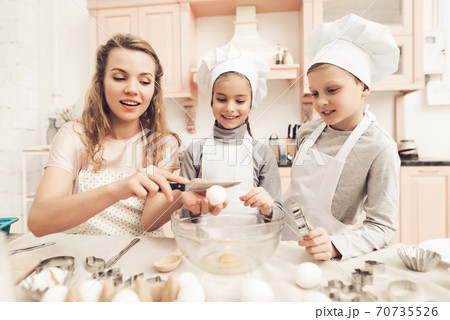 Mom helps daughter break eggs into the dishes. 70735526