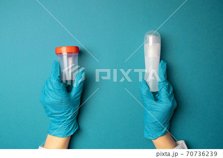 Doctor hands in latex rubber gloves holding a plastic container and a lubricant of liquids on blue background 70736239