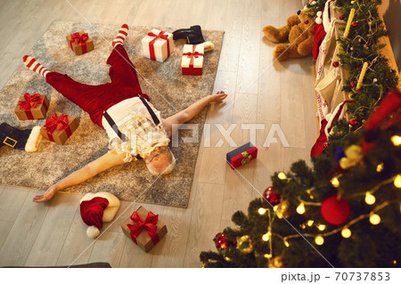 Drunk or simply tired Santa Claus sleeping on floor of a living-room with presents scattered around 70737853