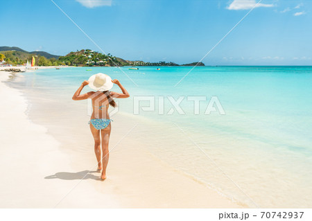 Beach travel vacation woman walking on luxury Caribbean cruise destination Antigua island in bikini wearing beach hat, carefree on holidays on Jolly Beach. Girl on travel vacation holidays swim model 70742937